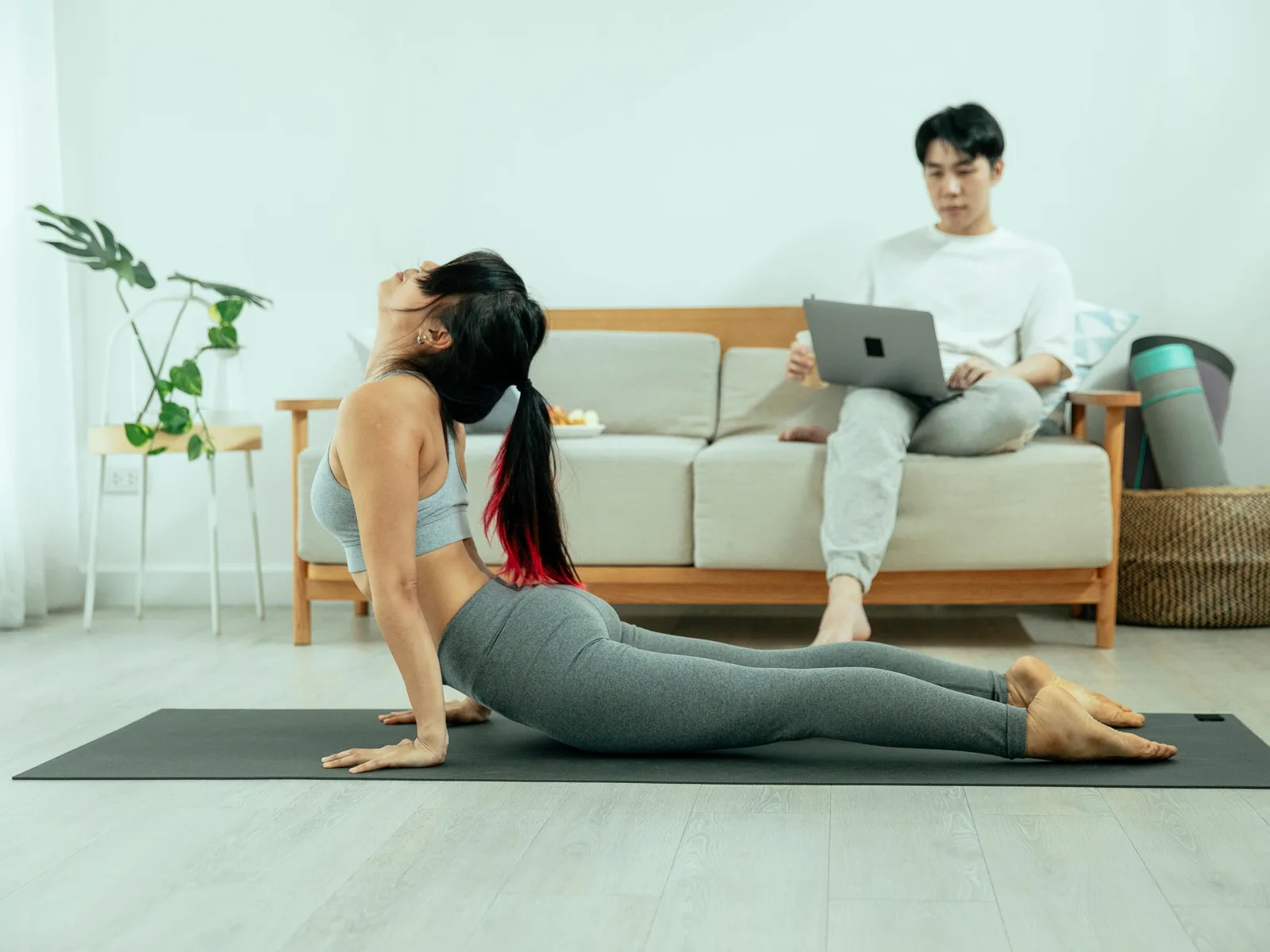 Une personne s’étire sur un tapis de sport dans un salon, devant un canapé.